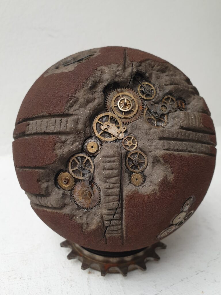 Human Rusty 2 di Cristian Bertolotto, scultura contemporanea in terracotta nera arrugginita con ingranaggi di vecchi orologi incorporati. Opera della serie Human, sfera artistica crepata e ricostruita a mano, simbolo delle avversità umane e della resilienza, con texture materiche ispirate all’Arte Povera.