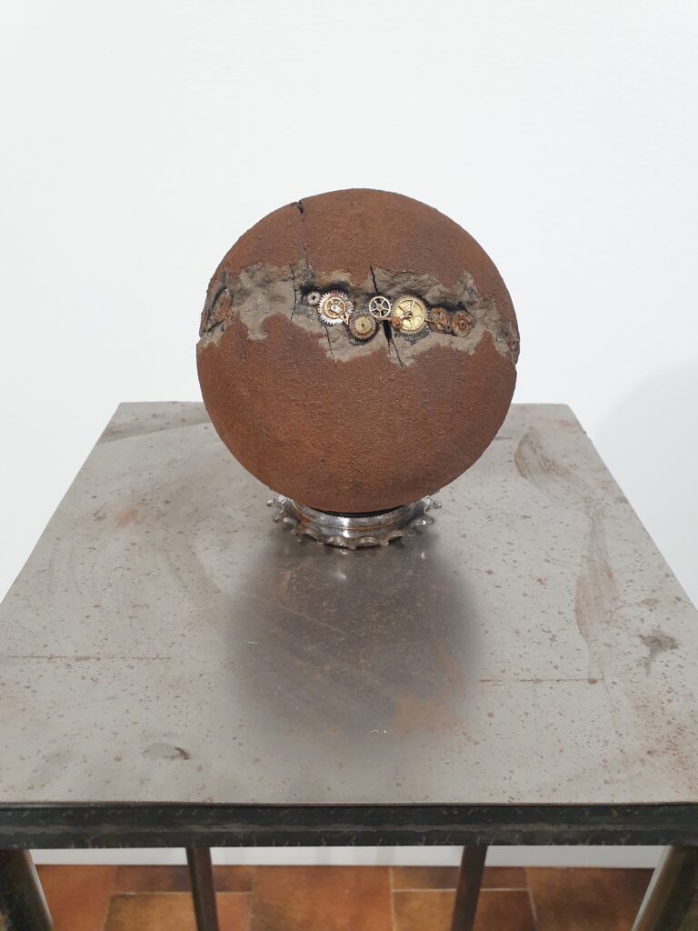 Human Rusty 1 di Cristian Bertolotto, scultura contemporanea in terracotta nera arrugginita con ingranaggi di vecchi orologi incorporati. Opera della serie Human, sfera artistica crepata e ricostruita a mano, simbolo delle avversità umane e della resilienza, con texture materiche ispirate all’Arte Povera.